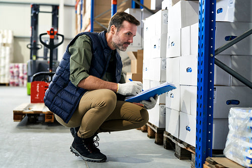Crouching caucasian men in mature age  checking documents and goods in warehouse