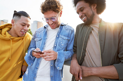 Three young men standing and scrolling a cell phone