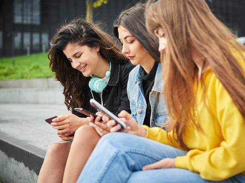 Side view of three girls using their smart phone