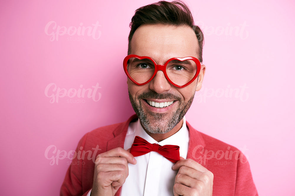 Cheerful man with heart shape eyeglasses adjusting a bow tie