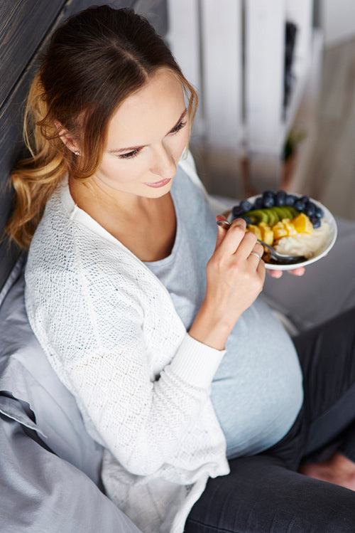 Pregnant woman having breakfast at bedroom