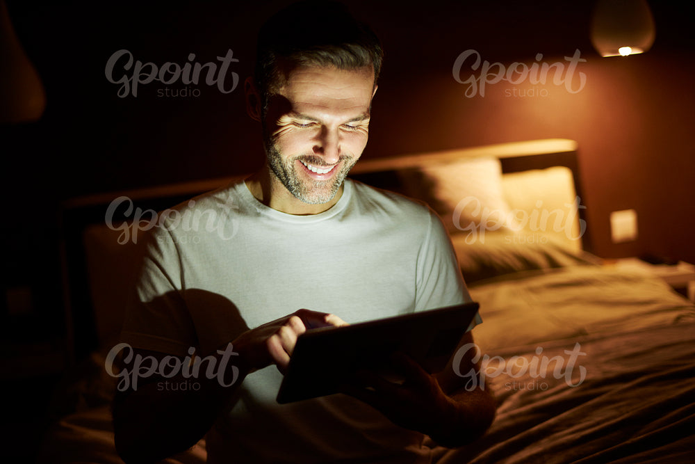 Smiling man using a  tablet at night