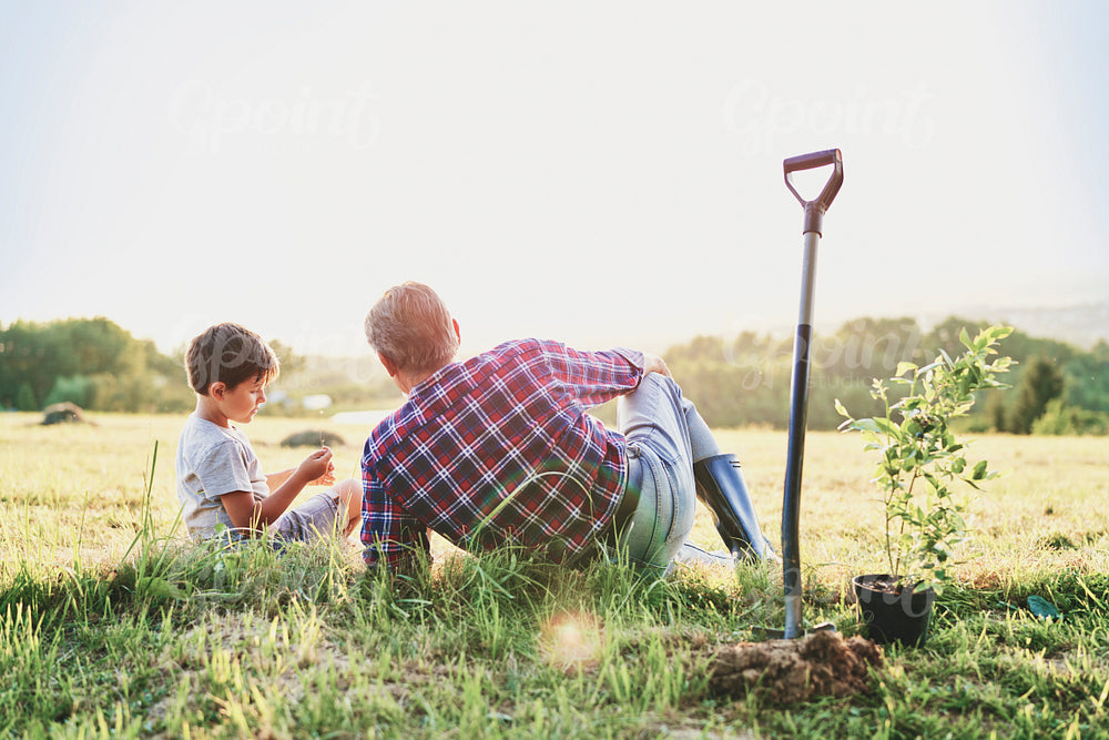 Grandpa and grandson sitting together in the meadow at sunset