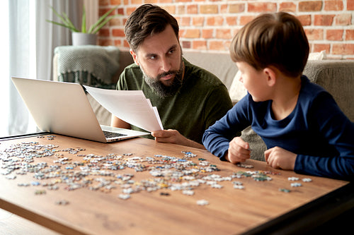 Father working and son solving jigsaw puzzle