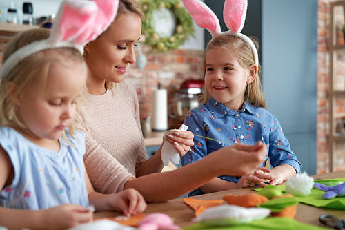 Mother teaches her little daughters sewing Easter decorations