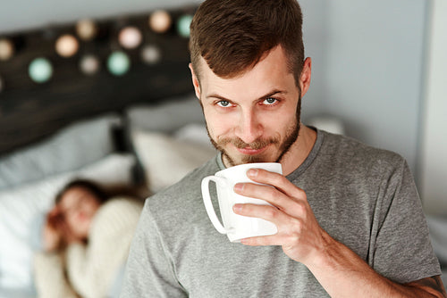 Front view of man drinking coffee in bedroom