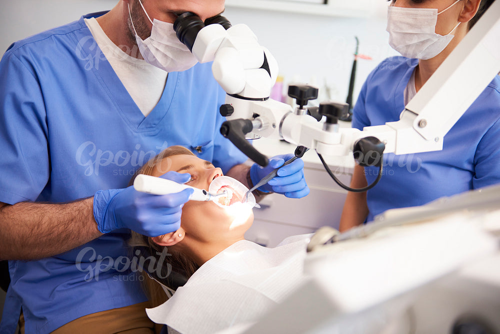 Dentist using dental microscope and examining woman's teeth