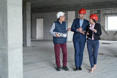 Wide image of group of caucasian engineers and investors walking and discussing on construction site