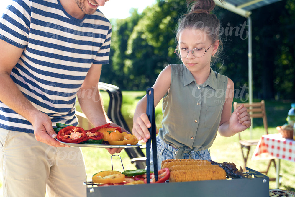 Daughter helping father with barbecue grill