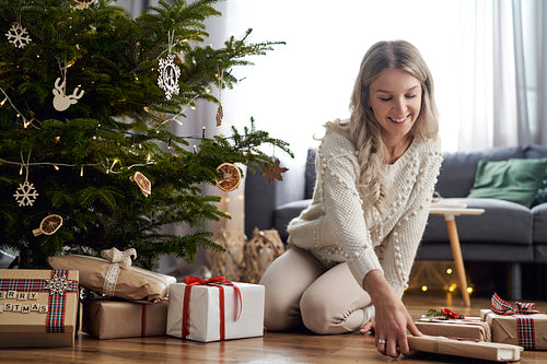 Young caucasian woman putting Christmas gifts under Christmas tree