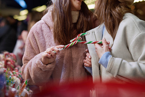 Two women buying  candy cane on Christmas market