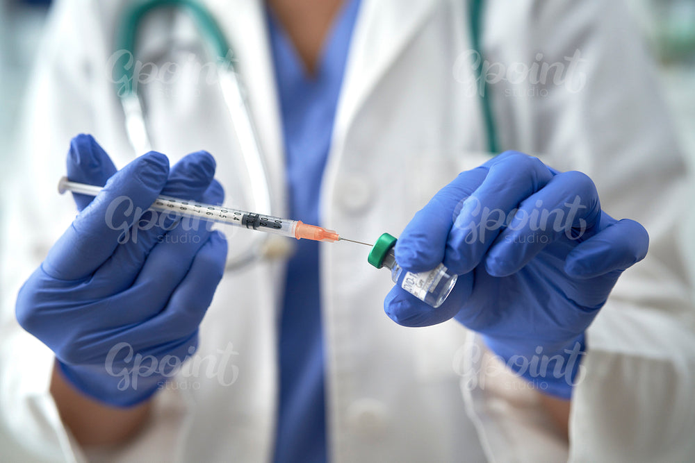 Close up of cropped hands inserting syringe into vial