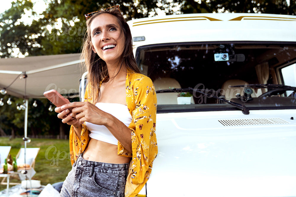 Young caucasian woman leaning on camper car, browsing mobile phone and looking away