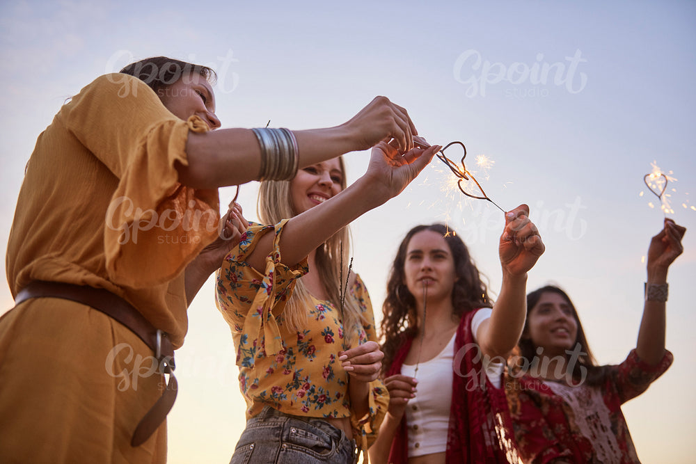Four young women with burning sparklers during sunset