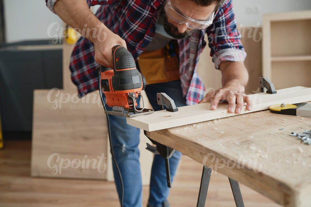 Carpenter in protective glasses sawing wood with an electric jigsaw