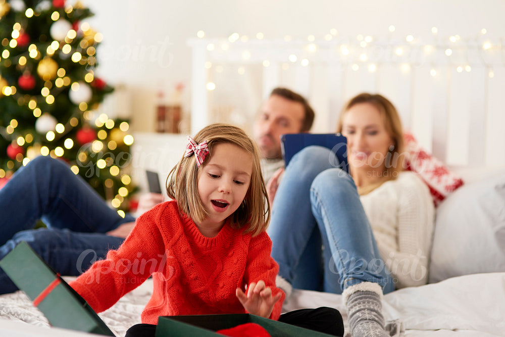 Child opening gift and parents with technology in the background