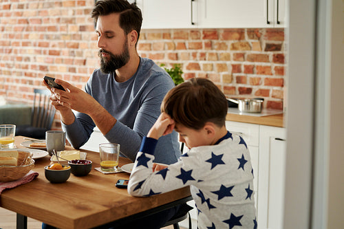 Father and son using mobile phone while breakfast