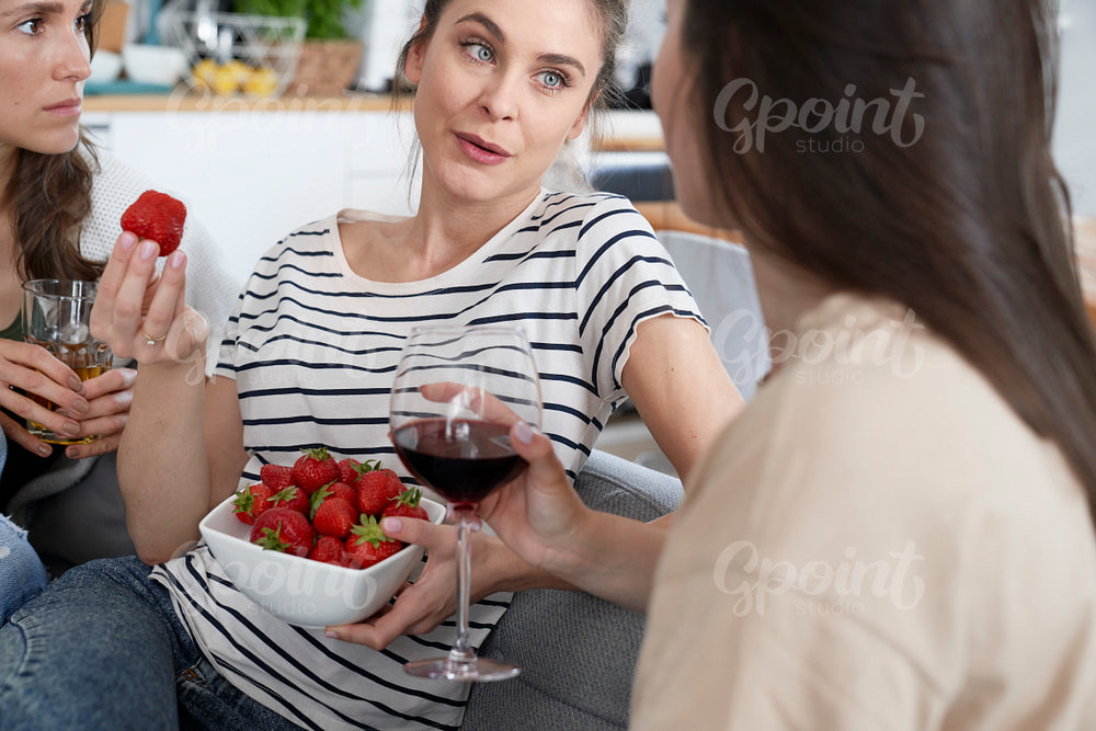 Three friends chatting and eating seasonal strawberries and drinking wine