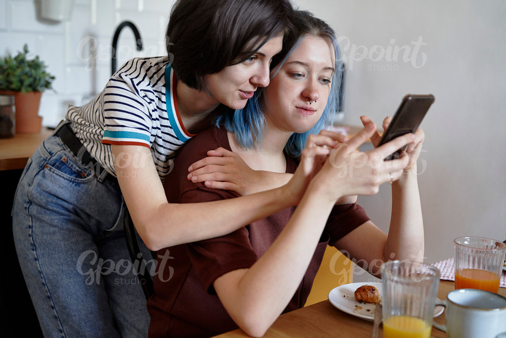 Lesbian couple browsing something on the phone during breakfast