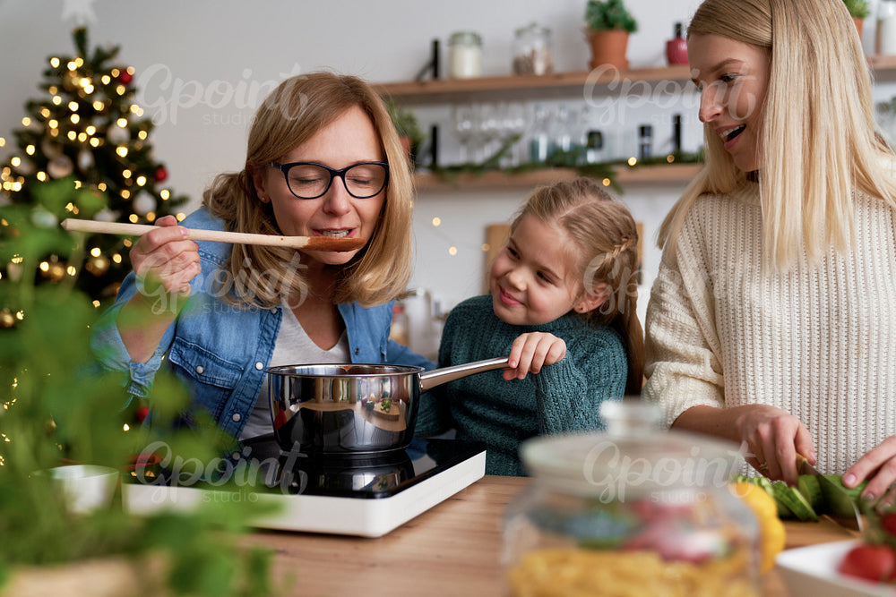 Grandma together with her daughter and granddaughter tasting Christmas dishes