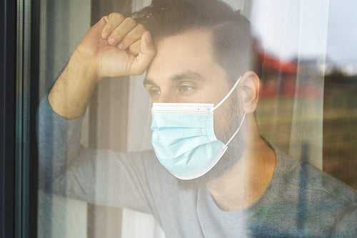 Resigned man with mask looking out of window