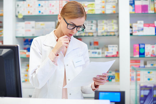 Female pharmacist checking documents at drugstore