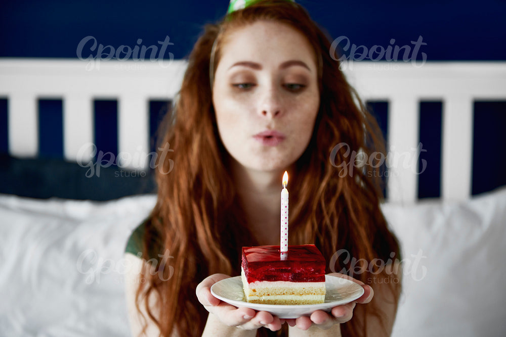 Redhead woman blowing a birthday candle on cake