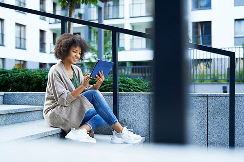 Woman sitting on city steps and scrolling on the tablet