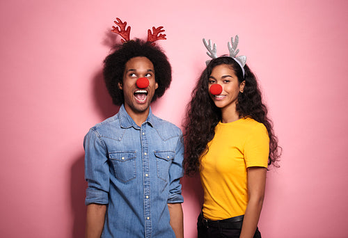 Young African couple standing in reindeer headbands and red nose.