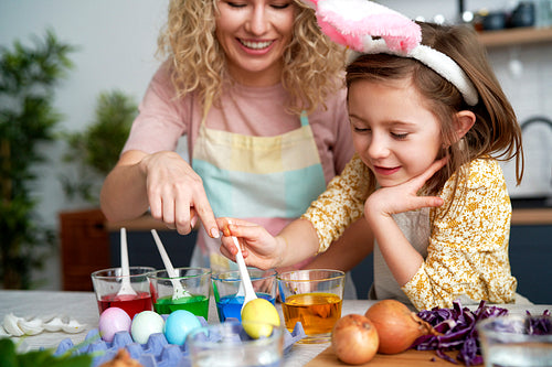 Mom and daughter dyeing Easter eggs in the kitchen