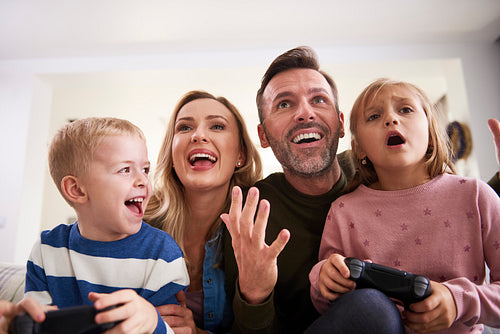 Emotional parents and children playing video game at home