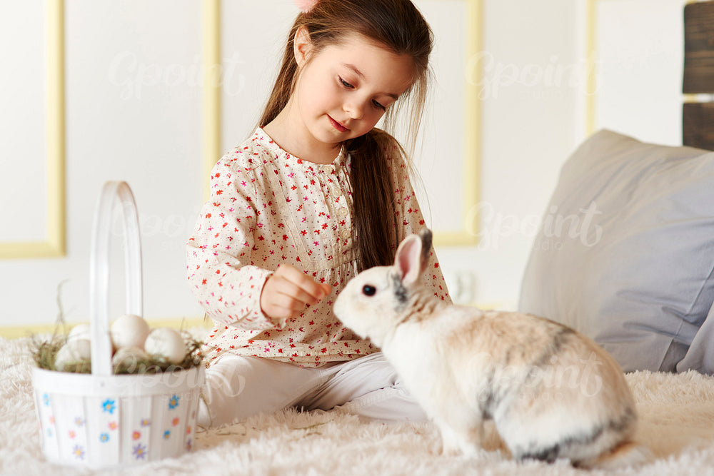 Small girl playing with rabbit on the bed