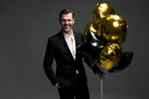 Studio shot of elegant middle aged caucasian man holding golden balloons