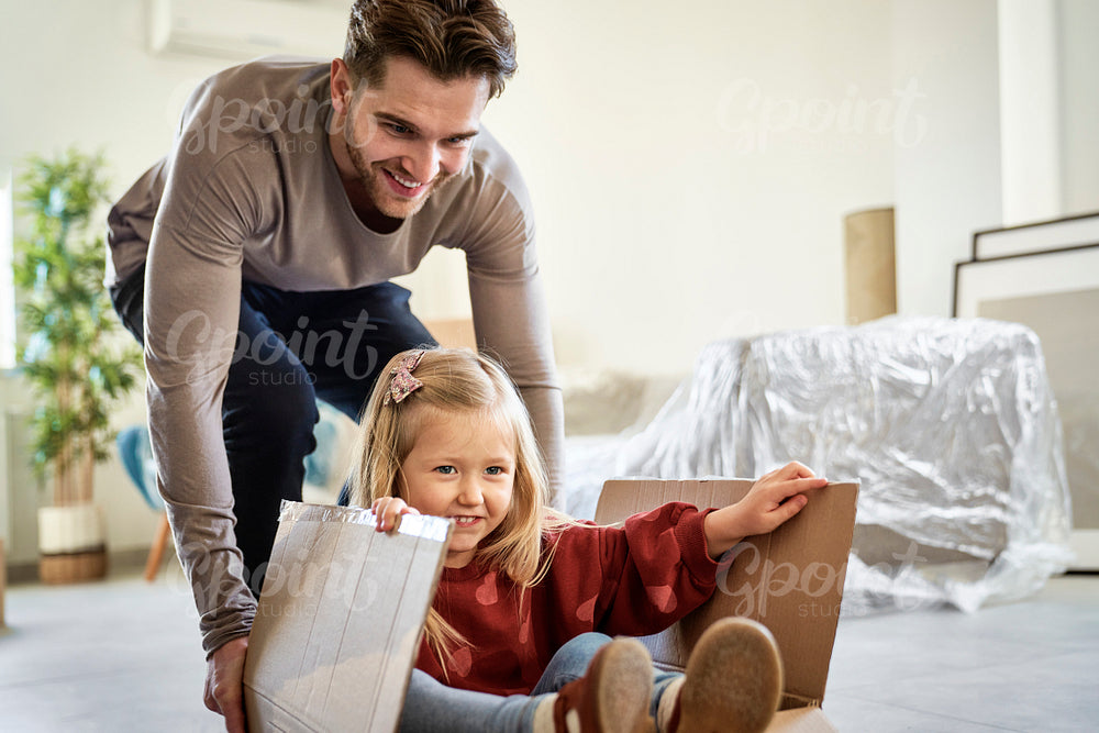 Caucasian father pushing little girl in paper box while moving house 
