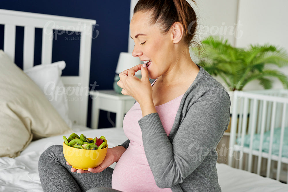 Cheerful pregnant woman eating a bowl of fruits
