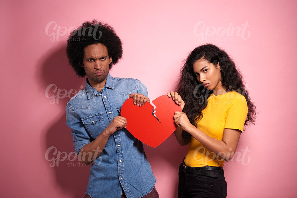 Sad African couple breaking the red heart in studio shot.