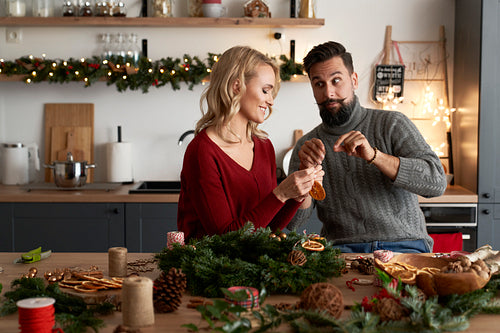 Couple decorating Christmas wreaths at table full of decorations