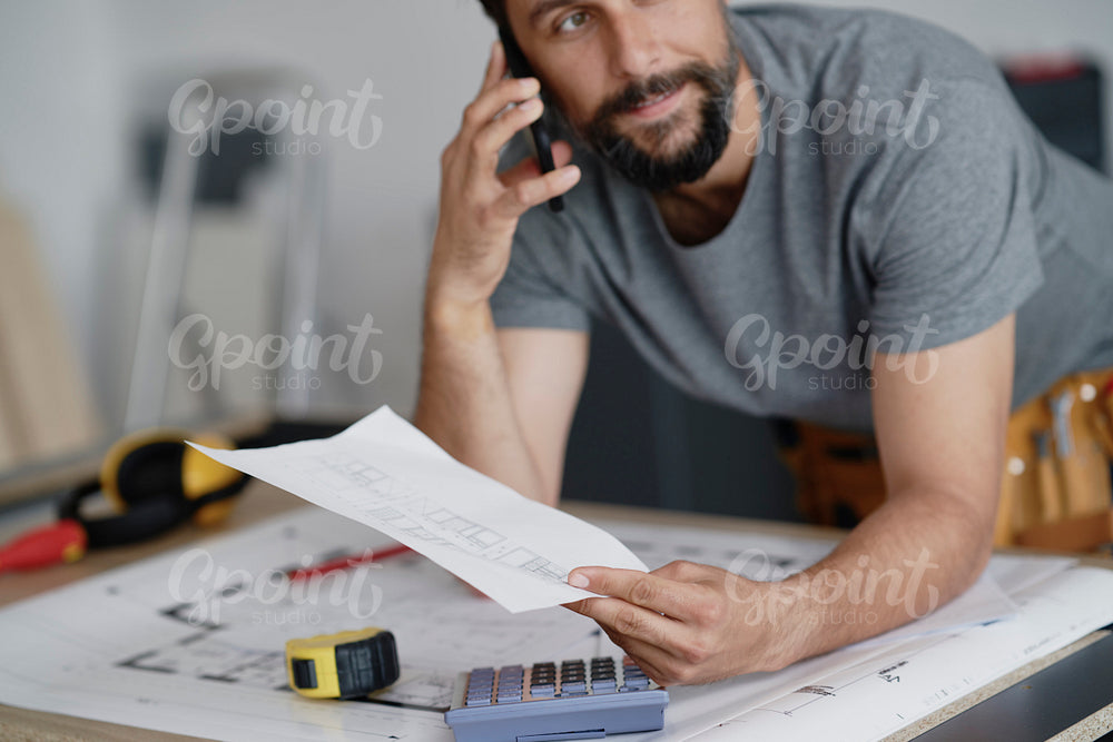 Carpenter holding plans and talking on the phone