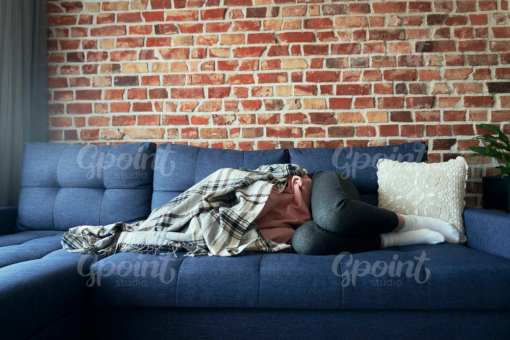 Woman with emotional problems lying on the couch and covered with a blanket   