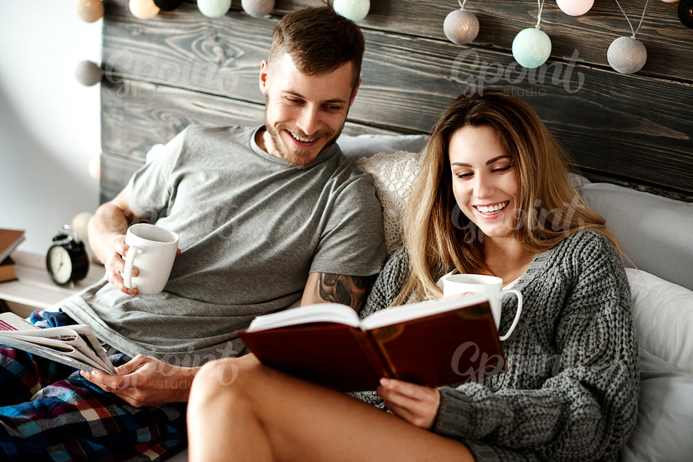 Happy young couple with coffee reading in bed