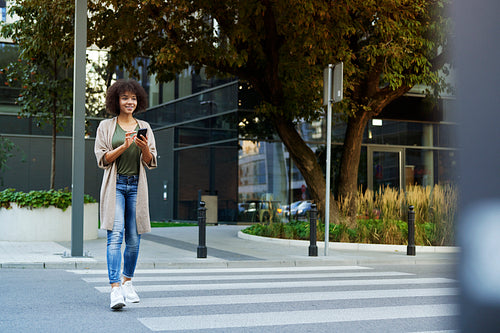 Smiling woman with mobile phone crossing the street