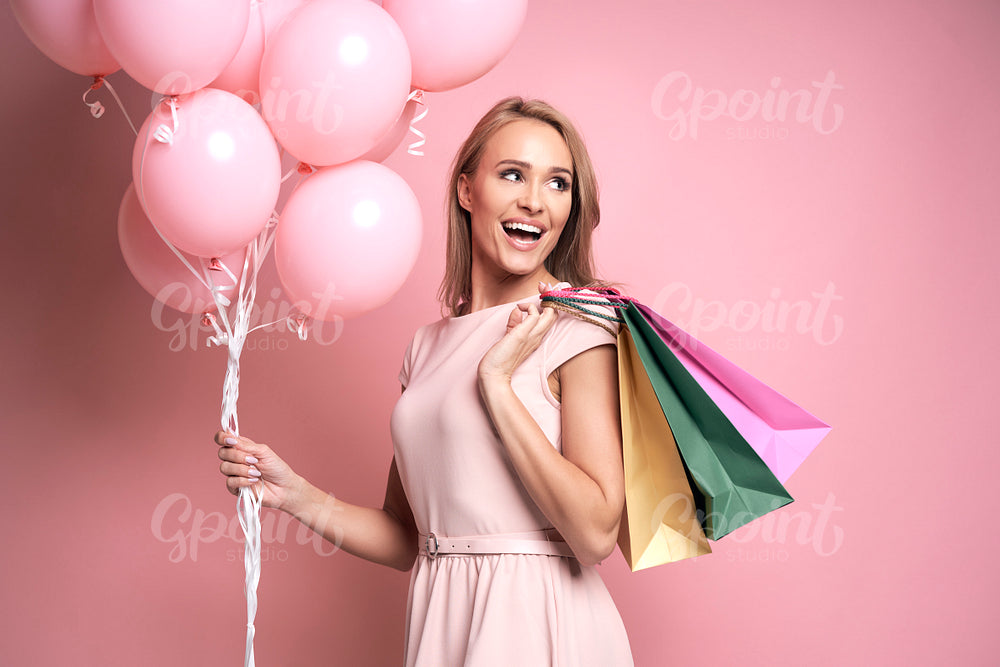 Studio shot of caucasian young woman with shopping bags and pink balloons