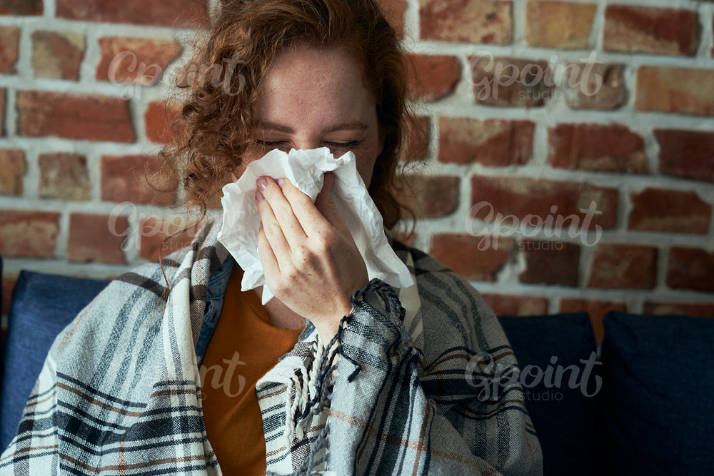 Caucasian woman blowing nose into tissue at home 