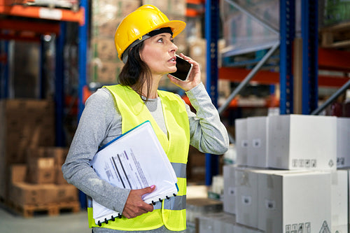 Adult caucasian woman talking on the mobile phone and looking up in warehouse