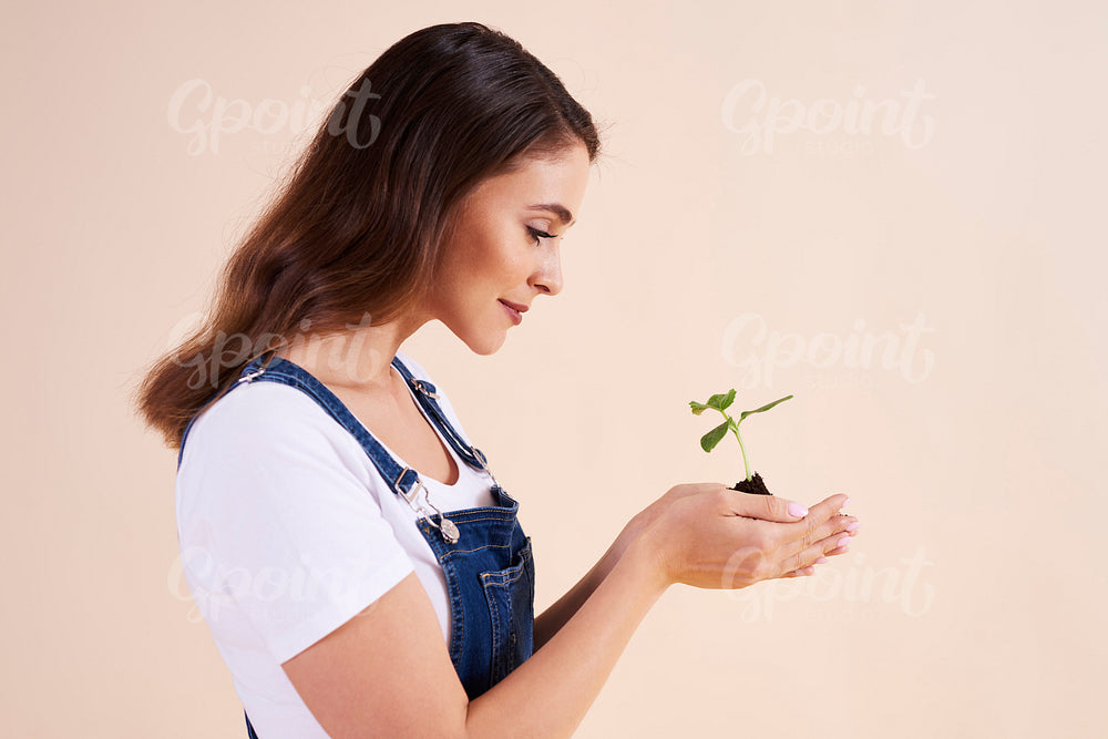 Side view of beautiful woman holding small seedling