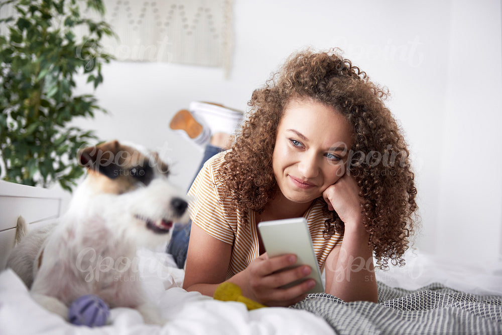 Young woman lying on the bed and using mobile phone