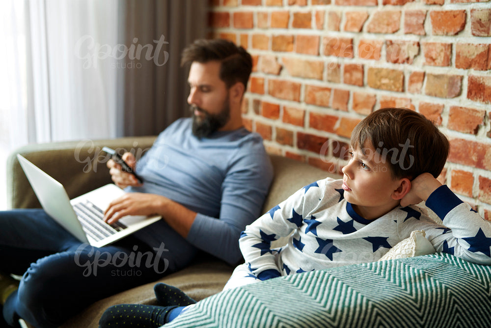Father working on the laptop and son watches TV