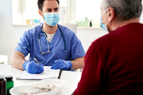 Doctor in protective face mask talking with a senior patient