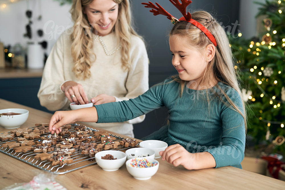 Caucasian mother and daughter decorating gingerbread cookies on Christmas time