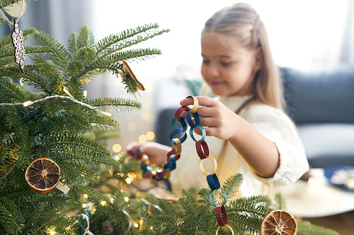 Caucasian little girl decorating Christmas tree with DIY paper chain